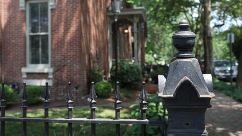 A closeup of a decorative cast iron fence outside a brick home at the corner of a brick sideawalk in Lockerbie Square neighborhood.
